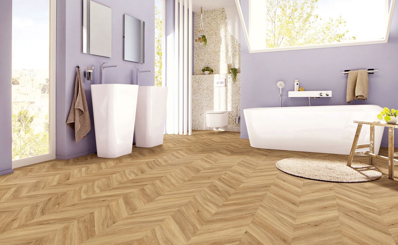 Modernes Badezimmer mit hölzernem Chevron-Boden, zwei Waschbecken, einer Badewanne und einer Toilette. Wände in lila und große Fenster.